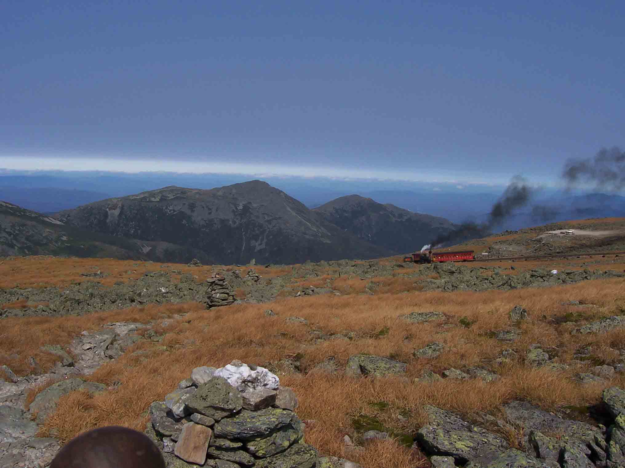 View north from north side of Mt. Washington.  Mts. Adams and Madison are visible. Note cog railway train descending the mountain. Taken from near the junction with the Great Gulf Trail at Mile 13.1.  Courtesy dlcul@conncoll.edu