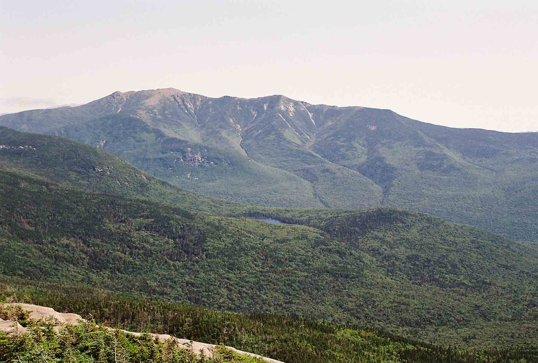 mm 5.4 - View east from North Kinsman Mt. The northbound AT descends to Lonesome Lake (center of picture), then continues descent into Franconia Notch.  It then climbs to the Franconia Ridge, reaching it somewhere near the far right of the picture.  The trail follow this ridge over Mt Lincoln and then Mt. Lafayette, the latter being the highest peak visible in the picture.   Courtesy dlcul@conncoll.edu